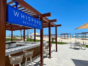 Un bar de playa llamado "Whispers Beach Bar", con barra, asientos y vistas a la playa.