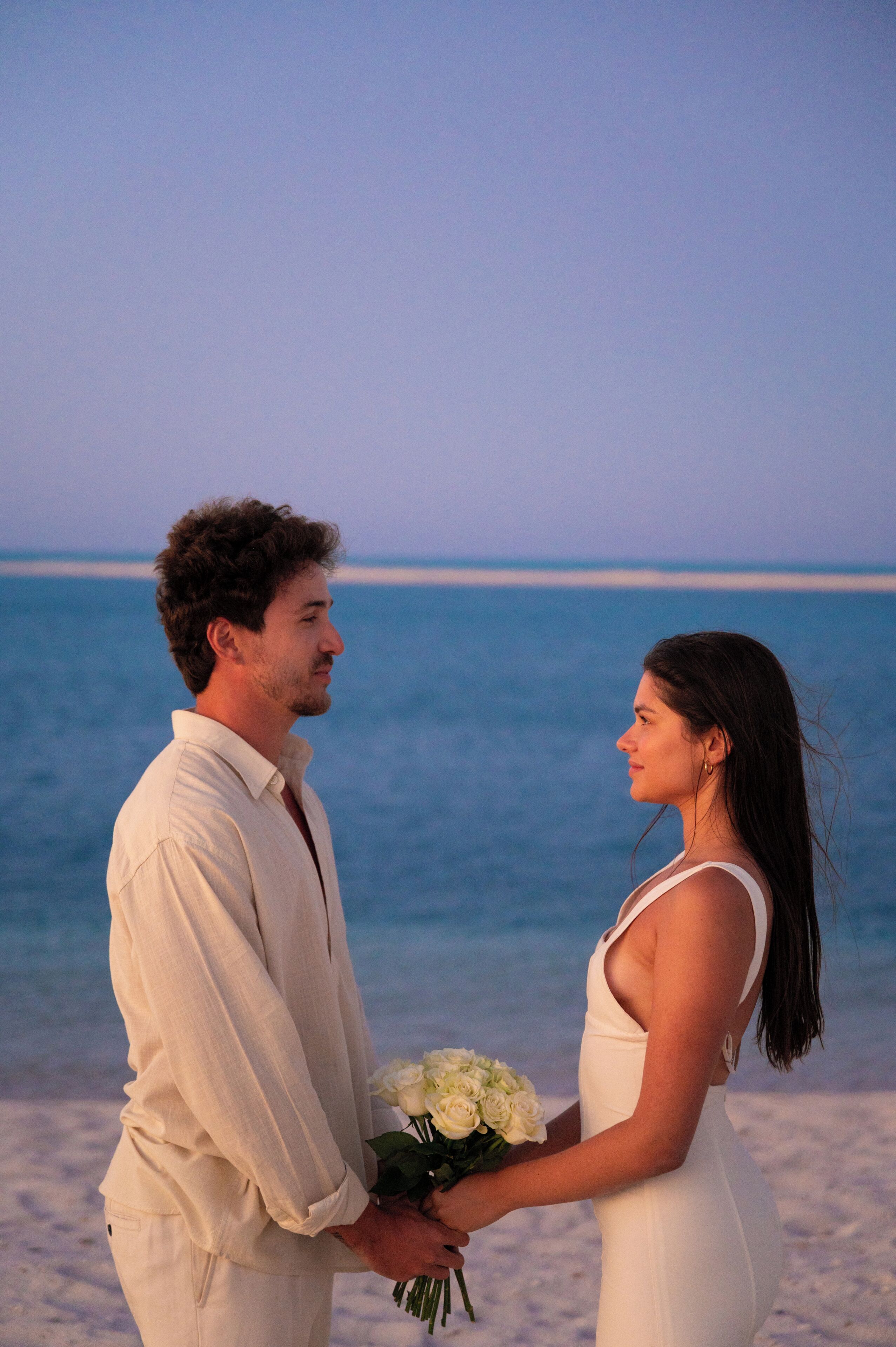 A couple holding hands on a beach with the ocean in the background.