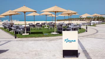 A beachside lounge area with multiple lounge chairs and umbrellas, a signboard with the name 'Nasma Lounge', and a clear view of the ocean.