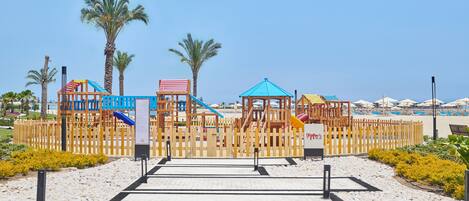 Un parque infantil con diversas estructuras de juego, una valla de madera y un cielo despejado.