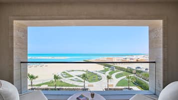 A balcony with a view of a beach and resort area, including a pool and palm trees.