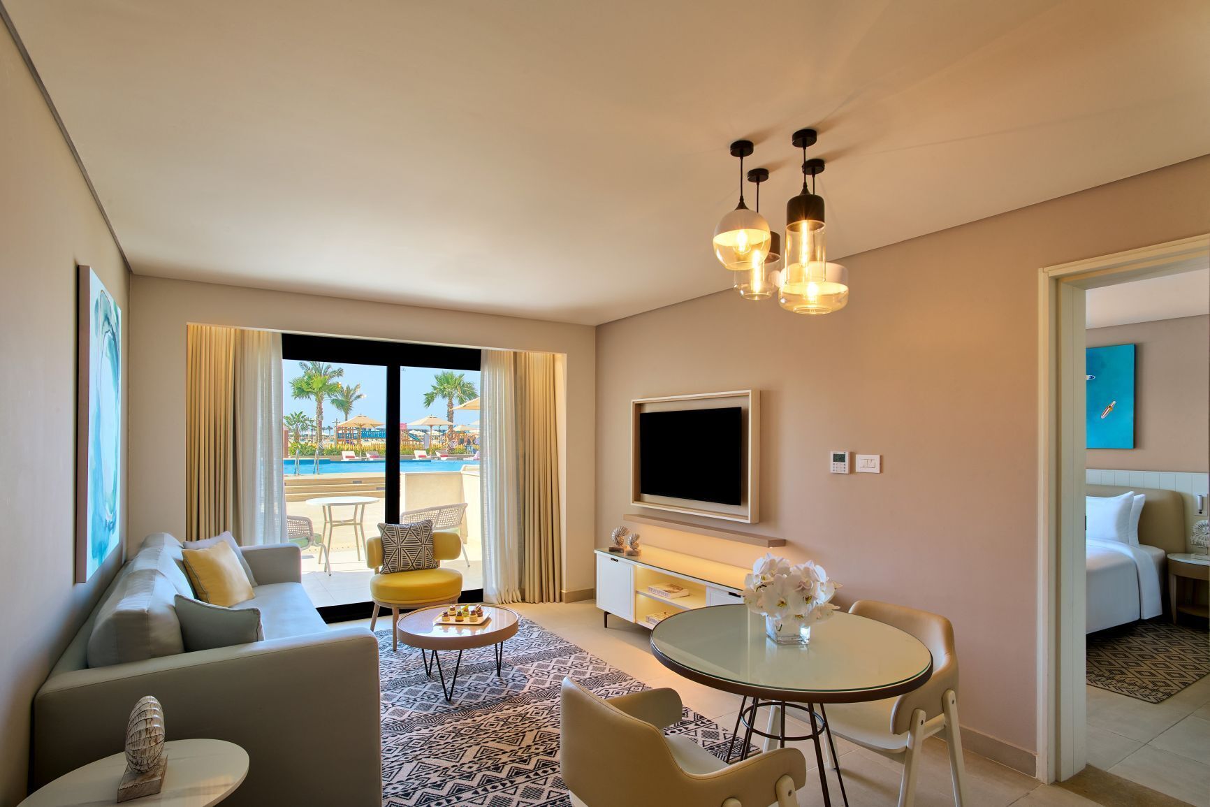 Habitación de hotel con sofá, mesa de comedor, televisor y vista a una piscina.