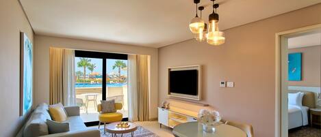 Habitación de hotel con sofá, mesa de comedor, televisor y vista a una piscina.