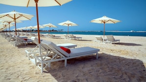 A beach with rows of white sun loungers and beige umbrellas.