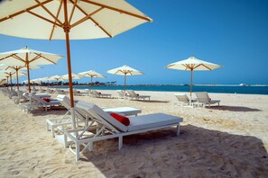 Una playa con filas de tumbonas blancas y sombrillas color beige.