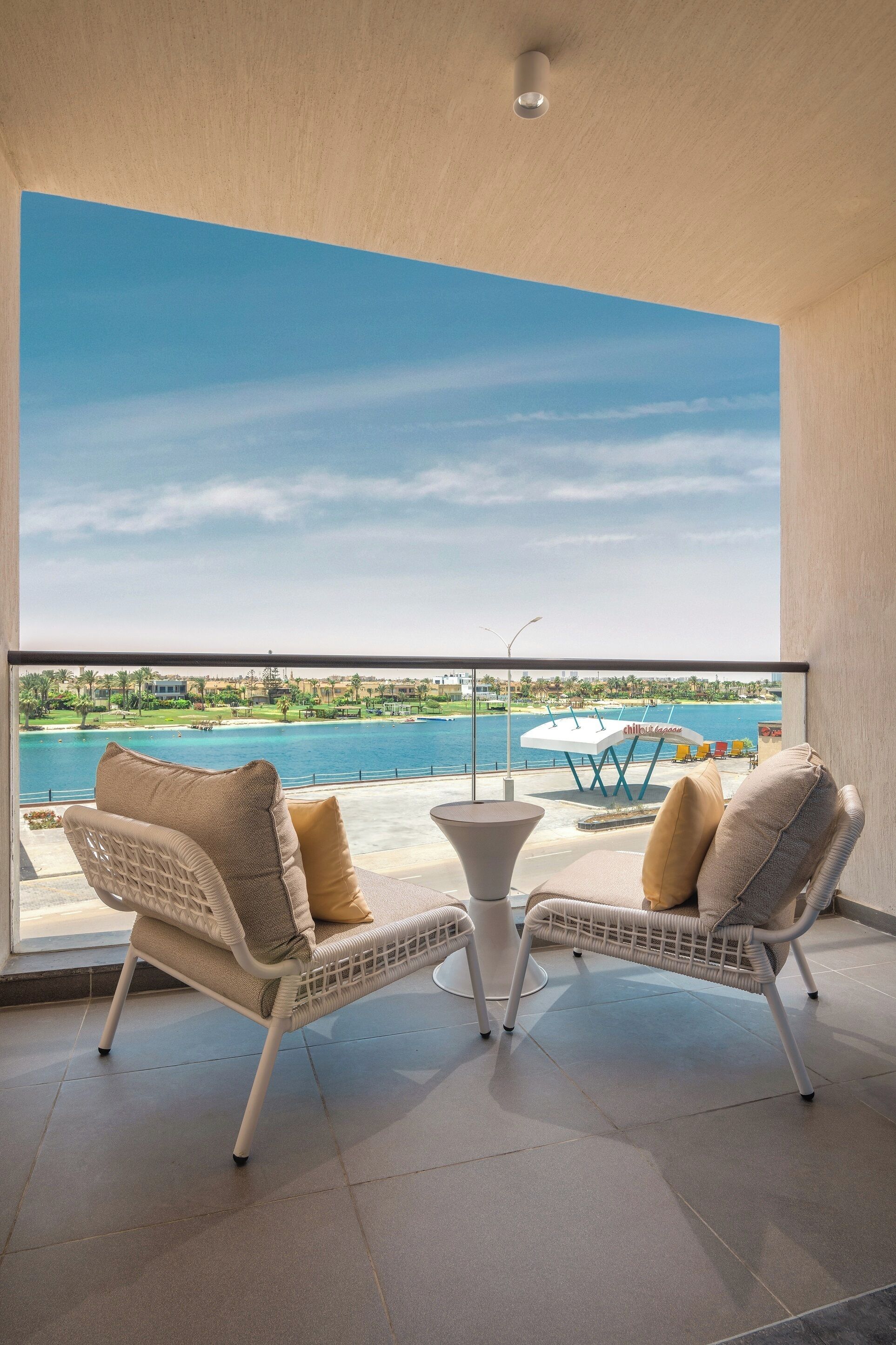 Un balcon avec deux fauteuils en osier et une petite table, donnant sur une étendue d’eau et une plage.
