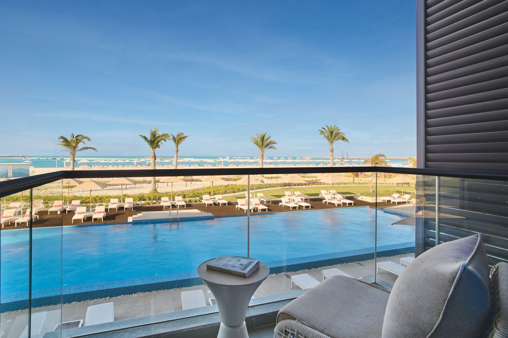 Un balcon avec une piscine, des chaises longues et une vue sur la plage et l’océan.