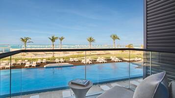 Un balcón con piscina, sillones de descanso y vistas a la playa y al océano.