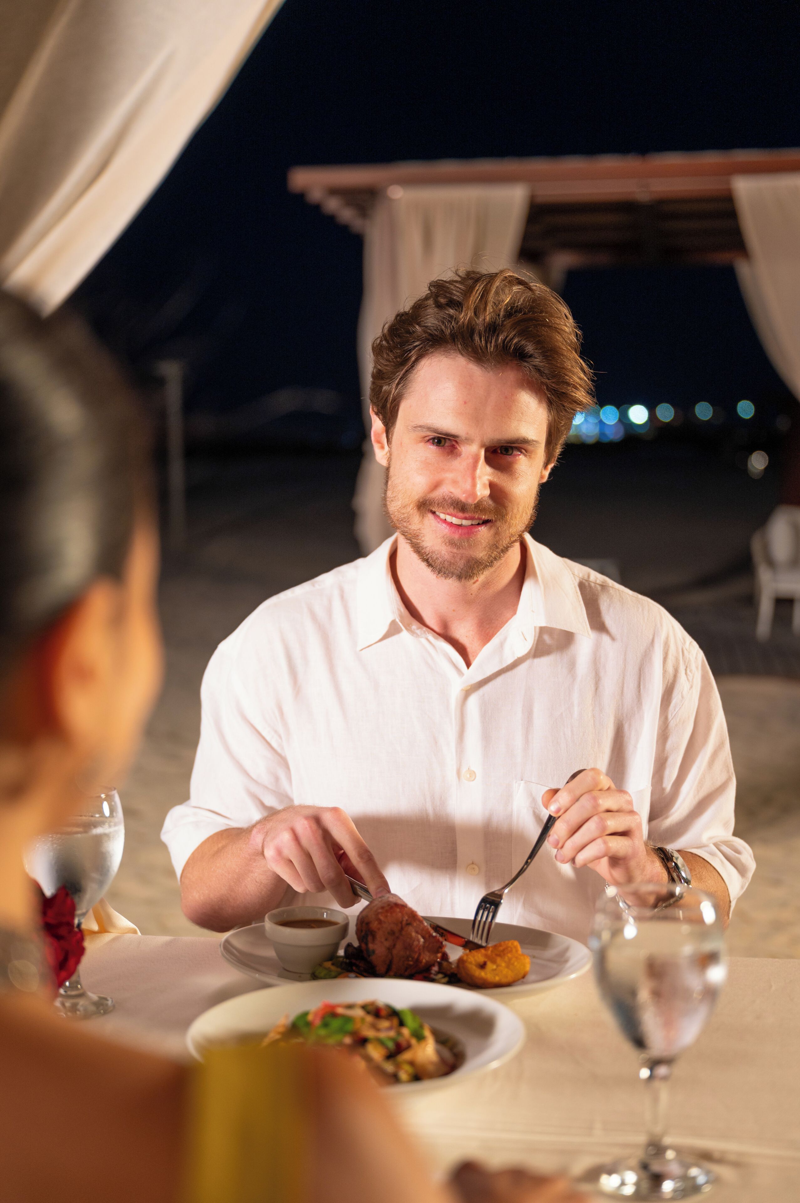 A person dining at an outdoor table with a plate of food, a glass of water, and a cup of coffee.