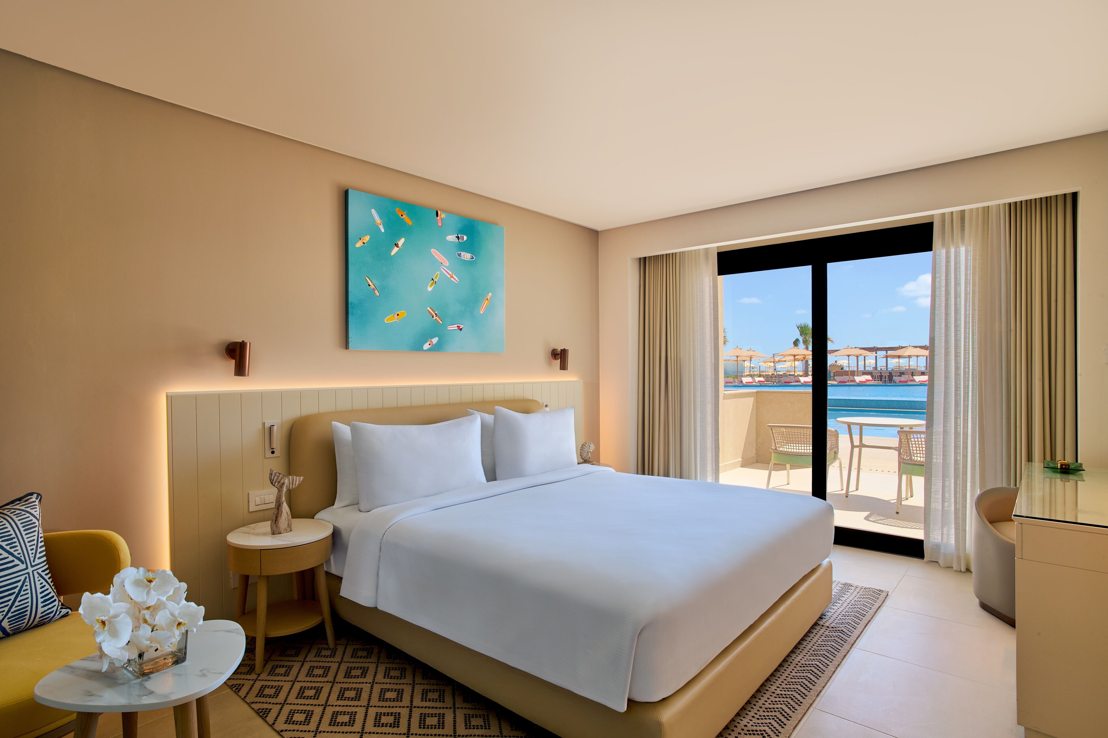 Habitación de hotel con una cama grande, vista al mar, un cuadro en la pared y una pequeña mesa con flores.