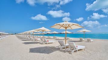 A beach with rows of sun loungers and umbrellas, a clear blue sky, and a calm sea.