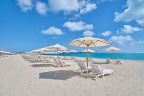 A beach with rows of sun loungers and umbrellas, a clear blue sky, and a calm sea.