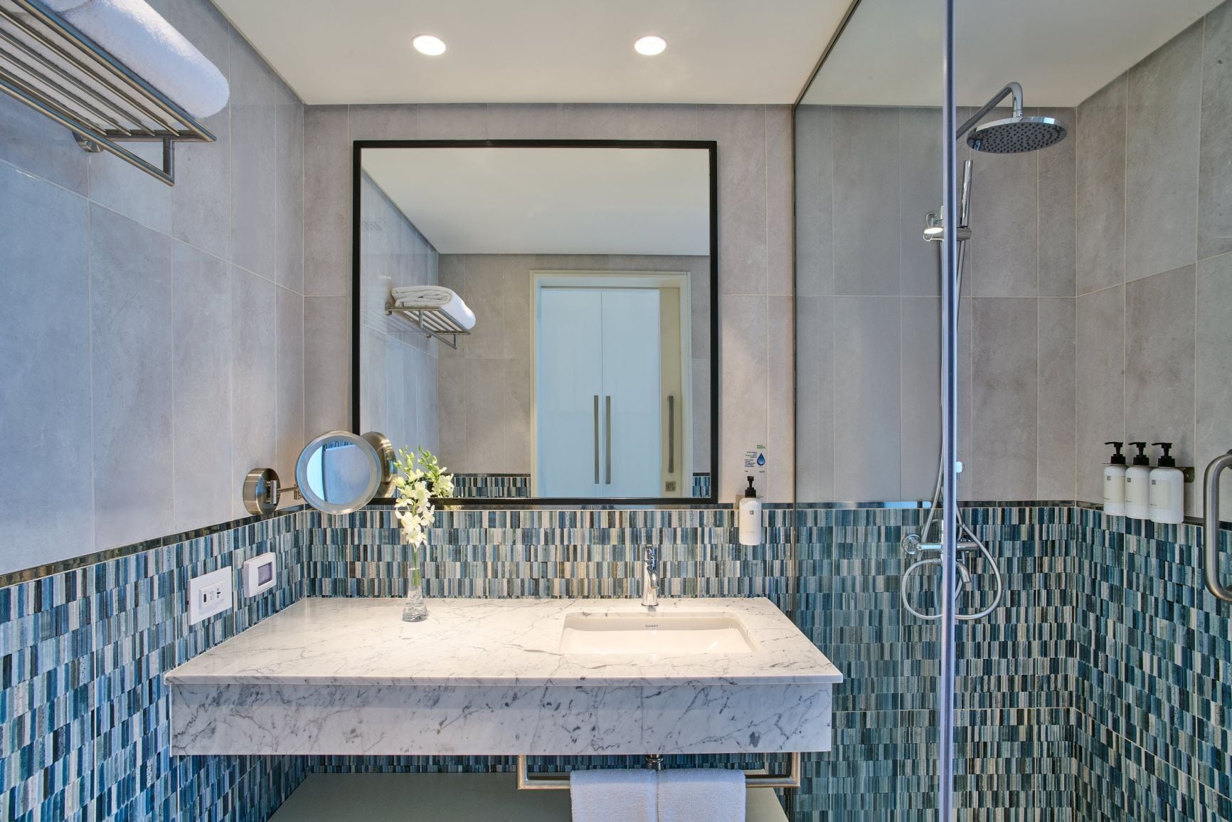 A modern bathroom with a marble sink, a large mirror, a shower, and a tiled backsplash.