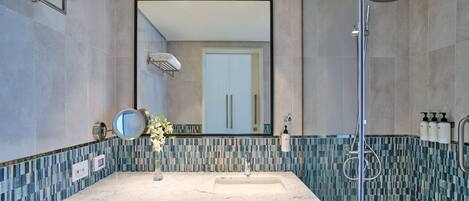 A modern bathroom with a marble sink, a large mirror, a shower, and a tiled backsplash.