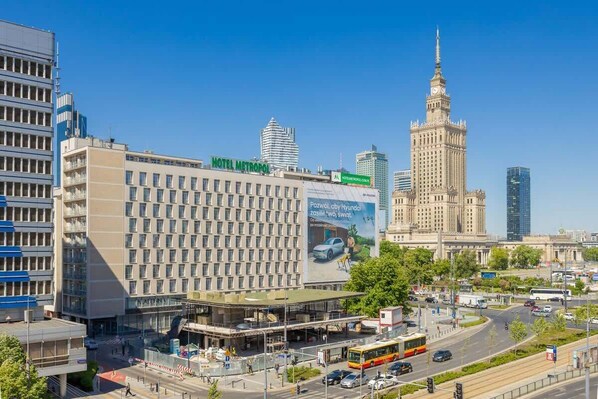 A hotel with a modern facade, a prominent clock tower in the background, and a clear blue sky. - Stylish Apartment in the Center | Balcony | View of the Palace of Culture and Science (Warszawa)