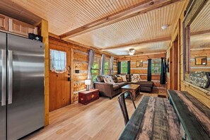 Ein Blockhauskamin mit Holzbalkendecke, einem Edelstahlkühlschrank, einer Couch und einem Esstisch.