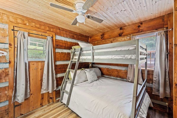 A cabin with a bunk bed, wooden walls, a ceiling fan, and curtains.
