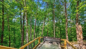 Un bain à remous sur une terrasse en bois, entouré d’une forêt.