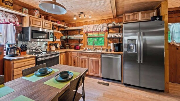 Une cuisine de style rustique, avec des éléments en bois, un coin repas, des appareils électroménagers en acier inoxydable et une vue sur la verdure environnante.