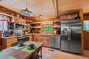 Una cucina in stile baita con elementi in legno, zona pranzo, elettrodomestici in acciaio inossidabile e vista sul verde circostante.
