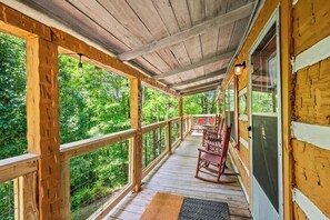 A wooden deck with a railing, wooden chairs, and a view of a forest.