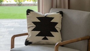 Una poltrona moderna con un cuscino a motivi geometrici, posizionata vicino a una finestra con tende, con vista su un giardino.