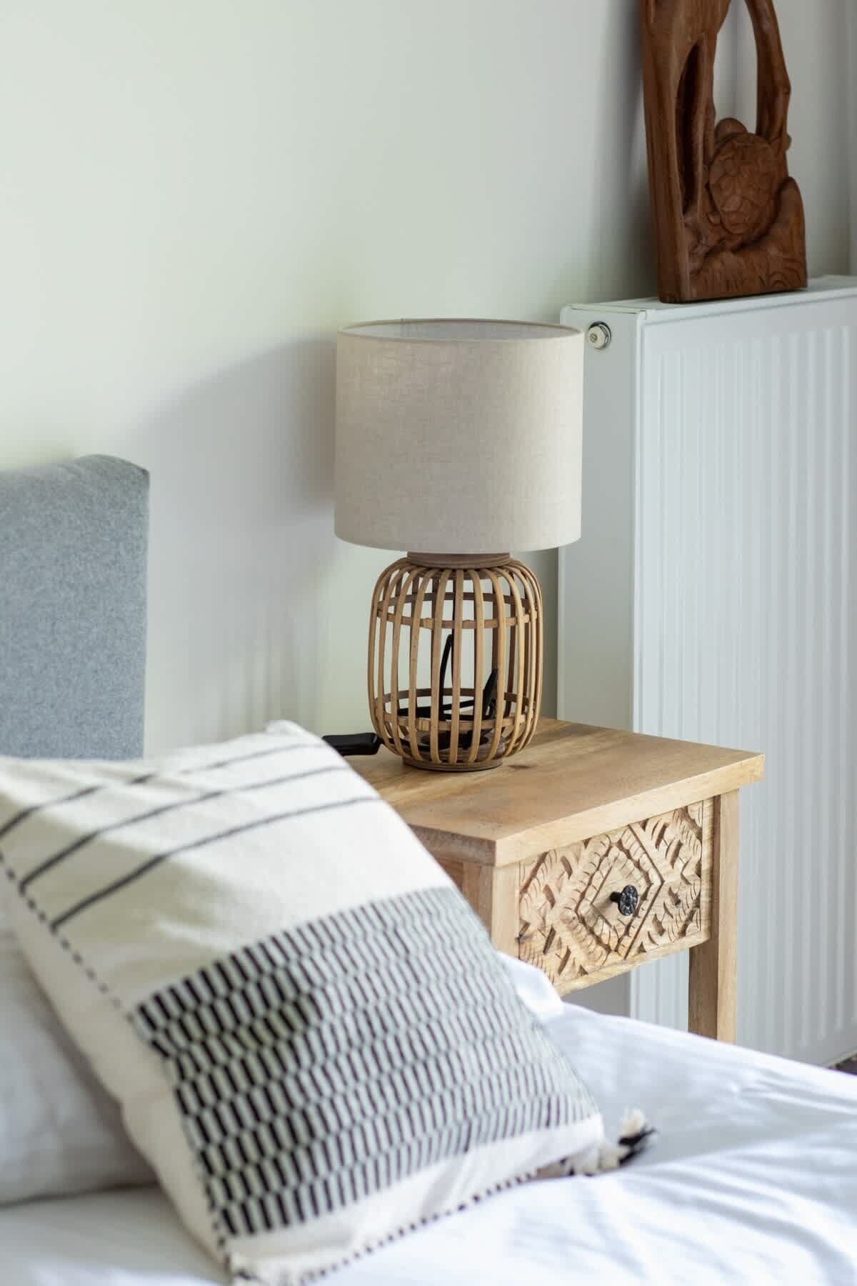 Ein Bett mit einem gestreiften Kopfkissen, ein Nachttisch aus Holz mit einer Lampe und ein Heizkörper im Hintergrund.