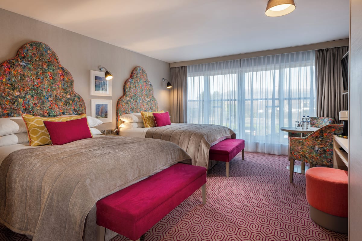 Habitación de hotel con dos camas, un escritorio y un ventanal con cortinas traslúcidas.