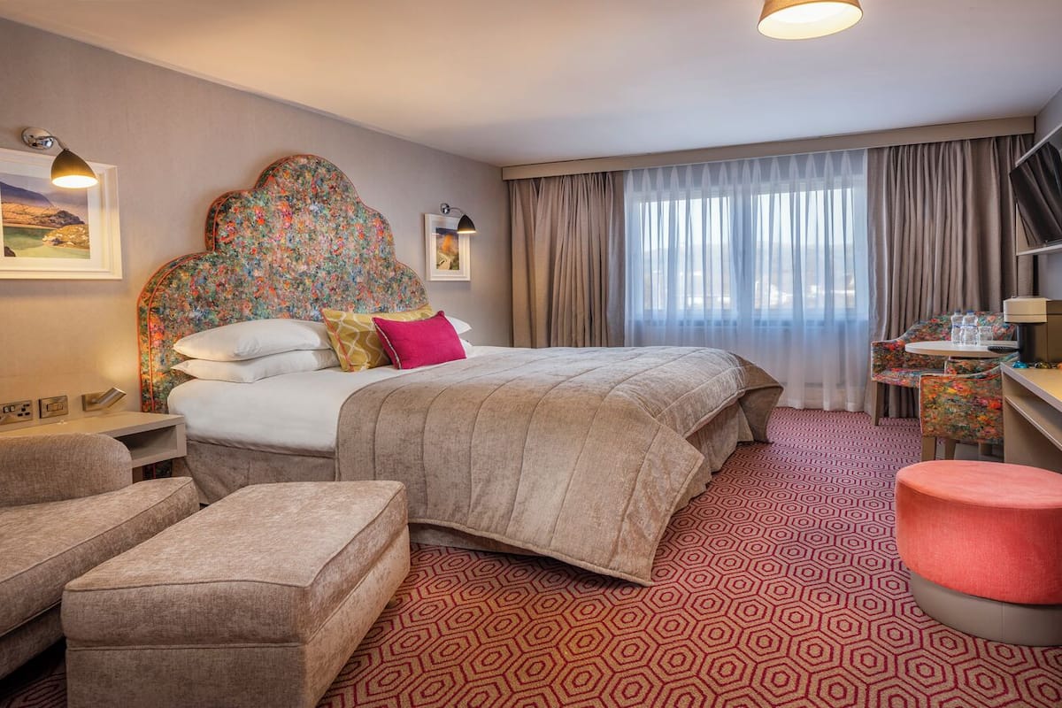 Una habitación de hotel con una cama grande, un escritorio, una silla, un sofá y un pequeño otoman.