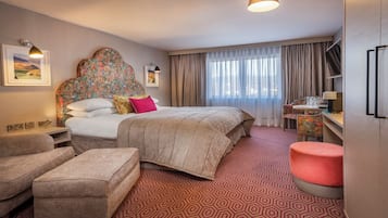 Una habitación de hotel con una cama grande, un escritorio, una silla, un sofá y un pequeño otoman.