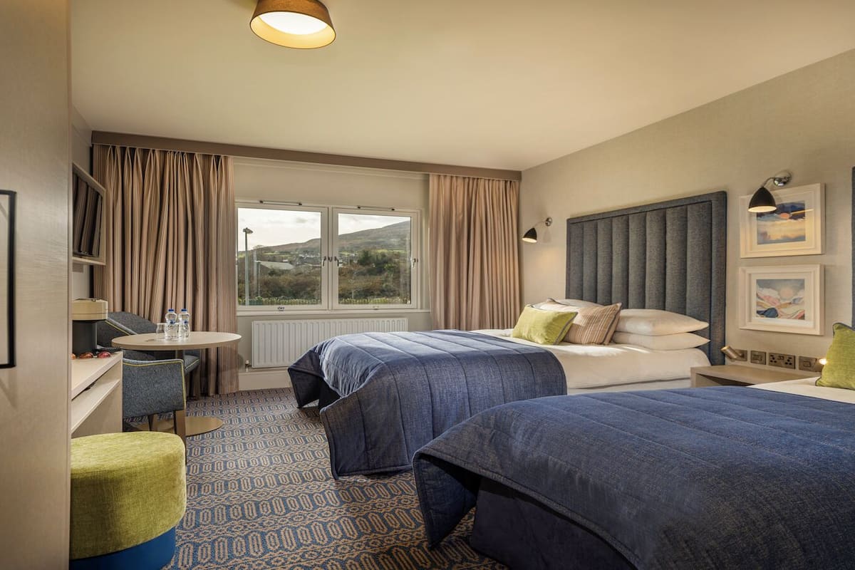 Habitación de hotel con dos camas, un escritorio, una silla, una mesa redonda y una ventana con cortinas.