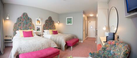 A hotel room with two beds, a desk, a mirror, and a TV.