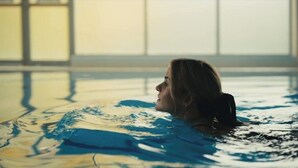 Una persona en una piscina con vistas a amplias ventanas al fondo.