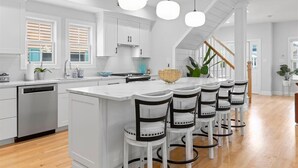 Une cuisine moderne avec un îlot central, des meubles blancs et un escalier en bois.