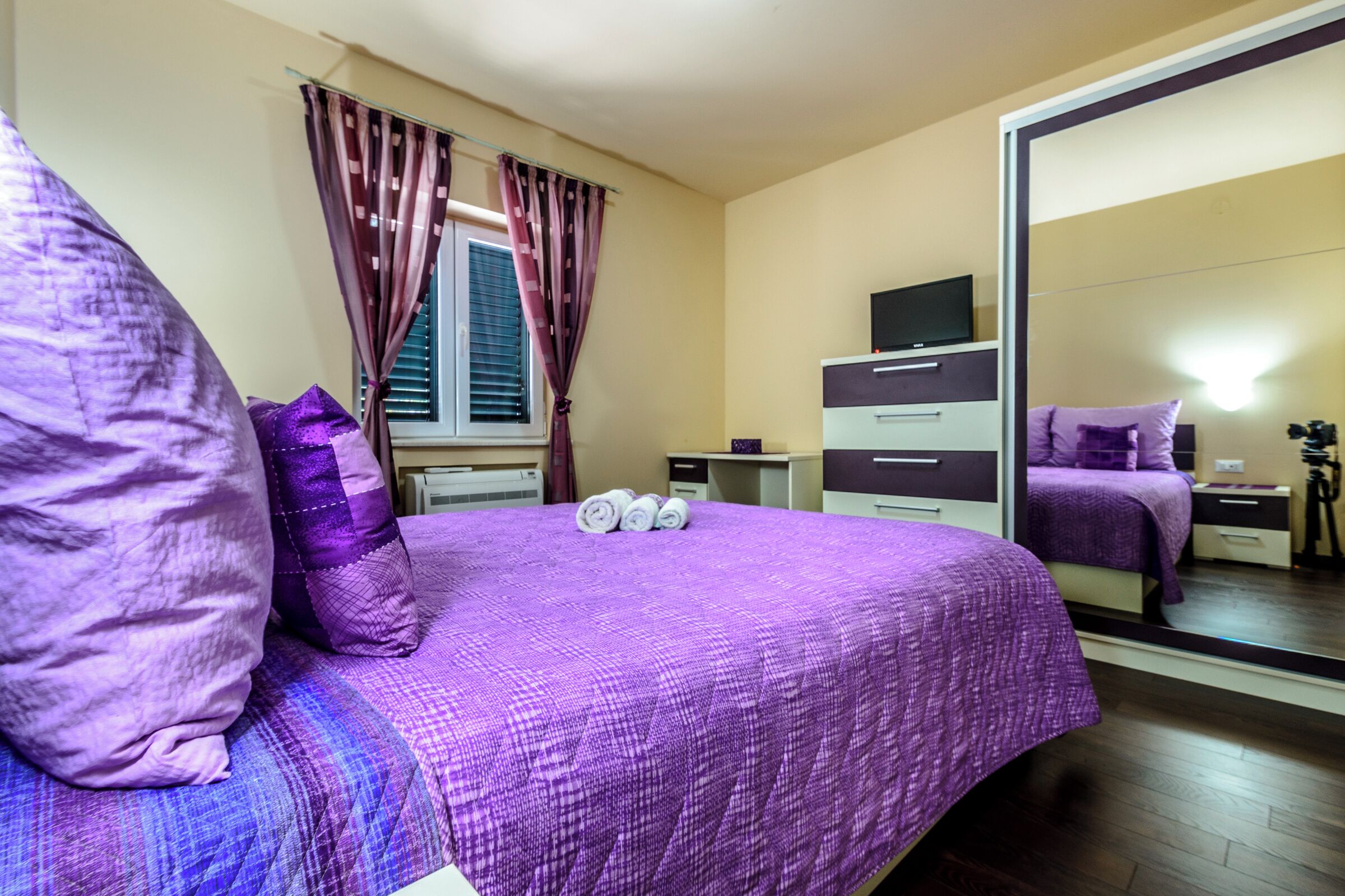 A bedroom with a large bed, a dresser, a TV, and a mirror.