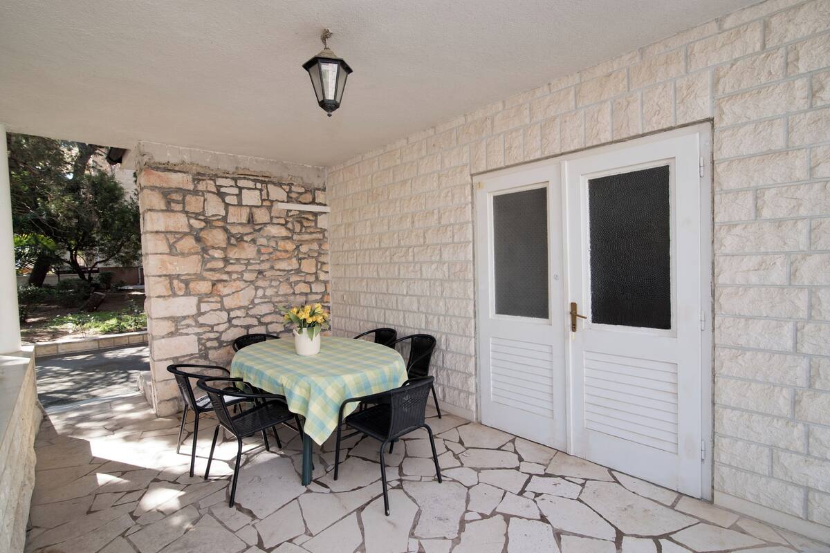 Un patio cubierto con una pared de piedra, una mesa con sillas y una puerta con ventanal.