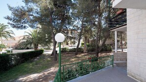 A paved pathway with a green metal railing, trees, and a white lamp post. - Apartments Pinija - (Supetar)