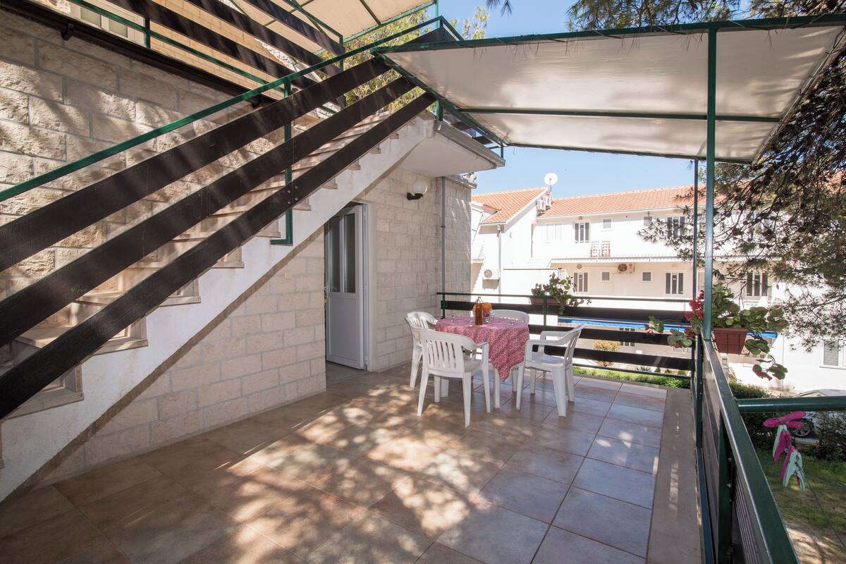 Un patio techado al aire libre con una mesa, sillas, una escalera y vistas a edificios vecinos.