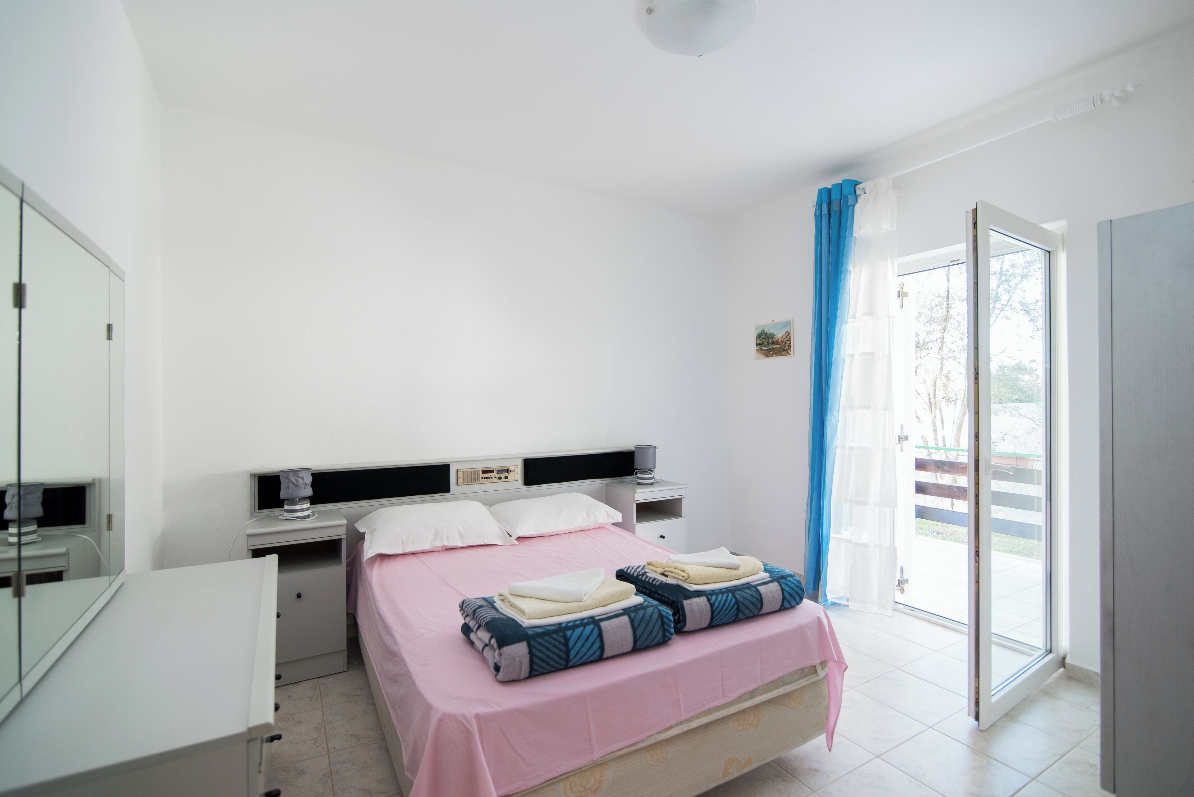 Een slaapkamer met een bed, nachtkastjes, een spiegel en een raam met gordijnen.