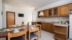 A compact kitchen with wooden cabinets, a built-in oven, and a small island with a sink. - Apartments Pinija - (Supetar)
