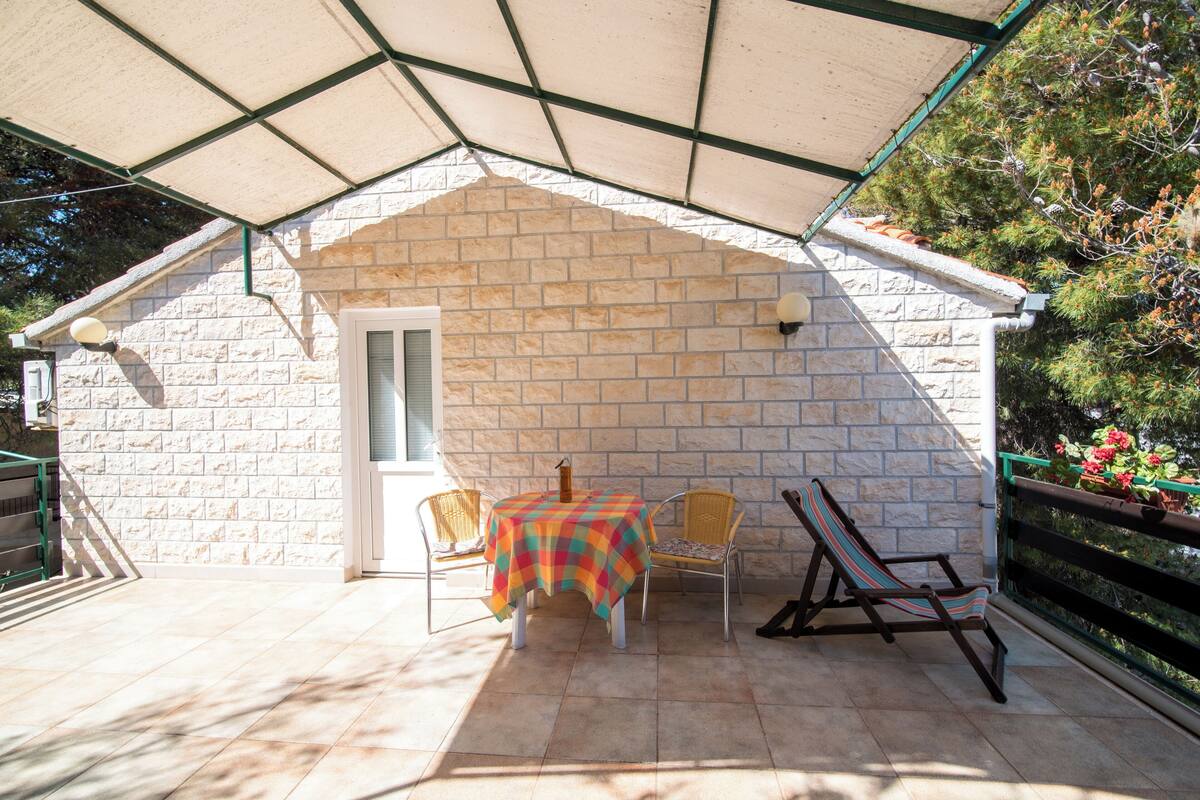 Un patio techado con mesa y sillas, un pequeño edificio de ladrillo y una terraza de madera.