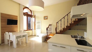 A modern kitchen with a dining area, wooden staircase, and a TV mounted on the wall. - Romantic Venetian Apartment with Grand Canal Views and High Ceilings (Venezia)