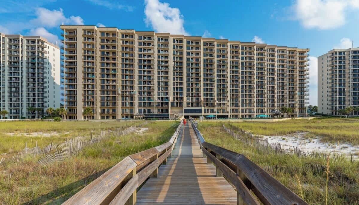 Une longue promenade en bois mène à un grand immeuble résidentiel doté de plusieurs étages et de balcons.