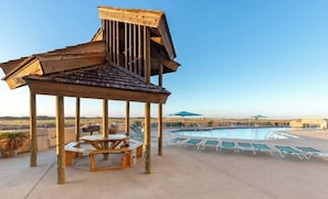 A wooden gazebo with a pool and lounge chairs.