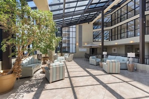 A spacious indoor area with a glass ceiling, multiple seating arrangements, and a large potted tree.
