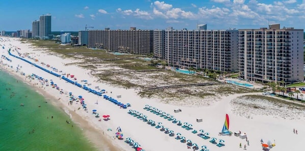 A beachfront hotel with multiple floors, a sandy beach, and a pool area.