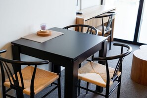 A modern dining area with a black table and chairs, a candle on the table, and a view of the outdoors through a large window.