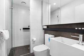 A modern bathroom with a glass shower enclosure, a white toilet, and a large mirror above the sink.