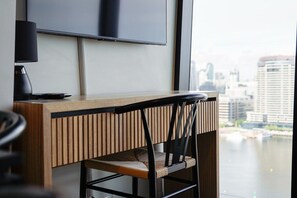 Una camera moderna con una scrivania in legno, una sedia nera e un'ampia finestra con vista sulla città.