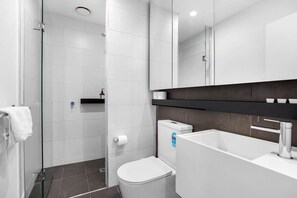 Ein modernes Badezimmer mit Duschkabine aus Glas, einer weißen Toilette und einem großen Spiegel über dem Waschbecken.